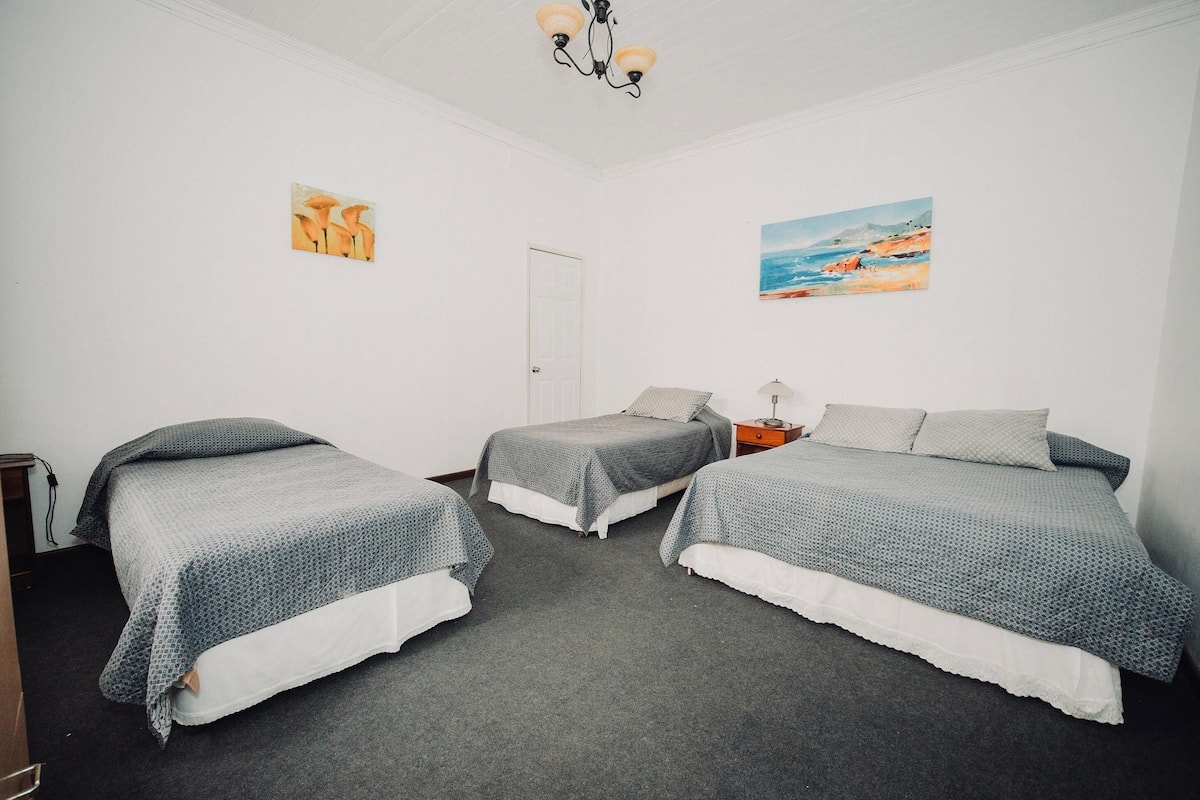 Una habitación con dos camas individuales, una mesita de noche, una lámpara y dos cuadros en las paredes.