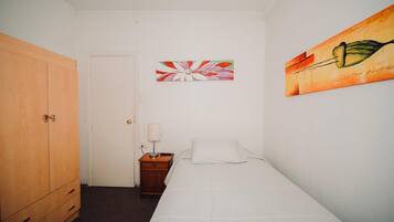 A bedroom with a single bed, a wooden wardrobe, a nightstand with a lamp, and two wall art pieces.