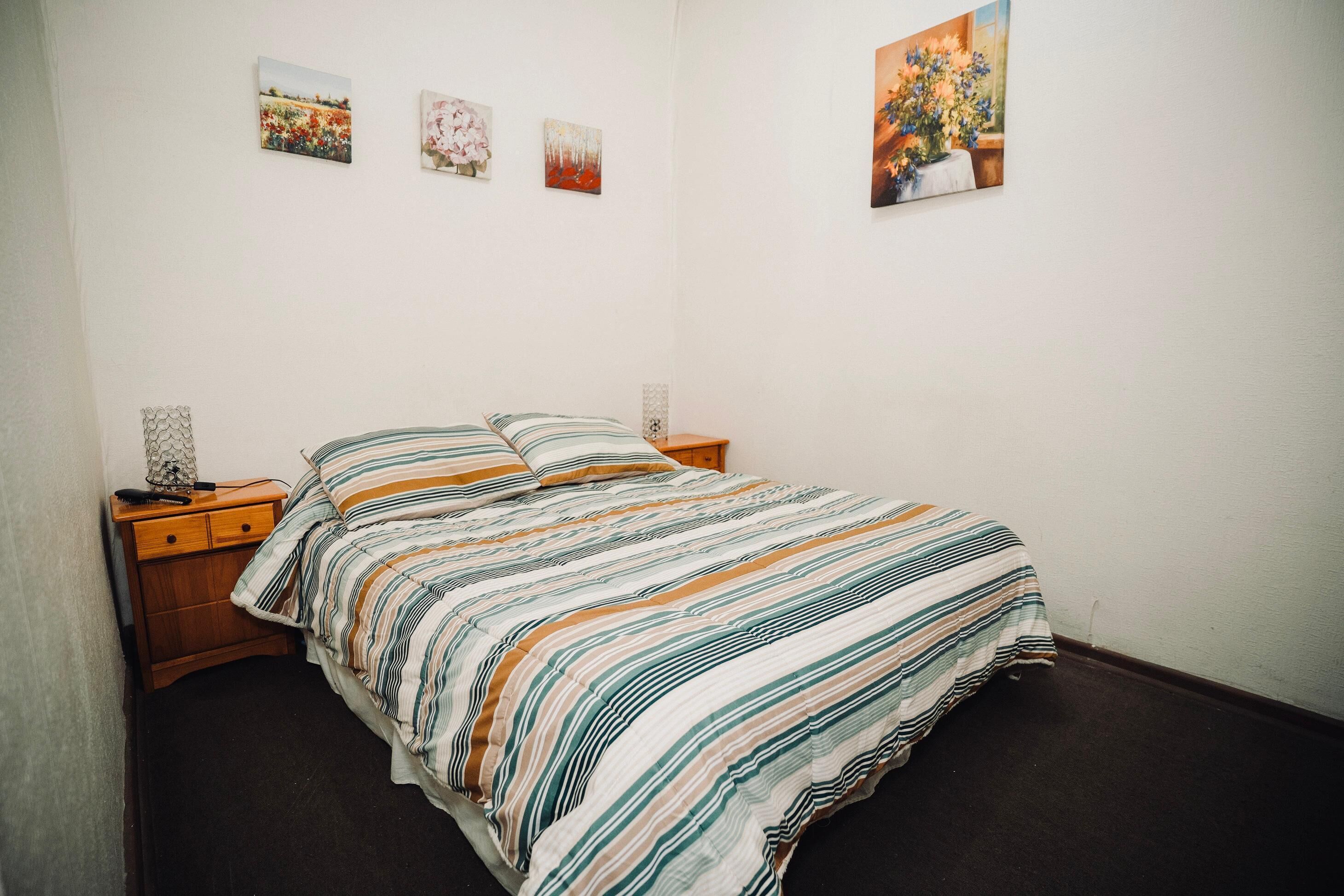 Ein Schlafzimmer mit einem Bett, einem Nachttisch und einer Wand mit drei gerahmten Bildern.