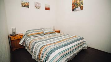 A bedroom with a bed, a nightstand, and a wall with three framed pictures.