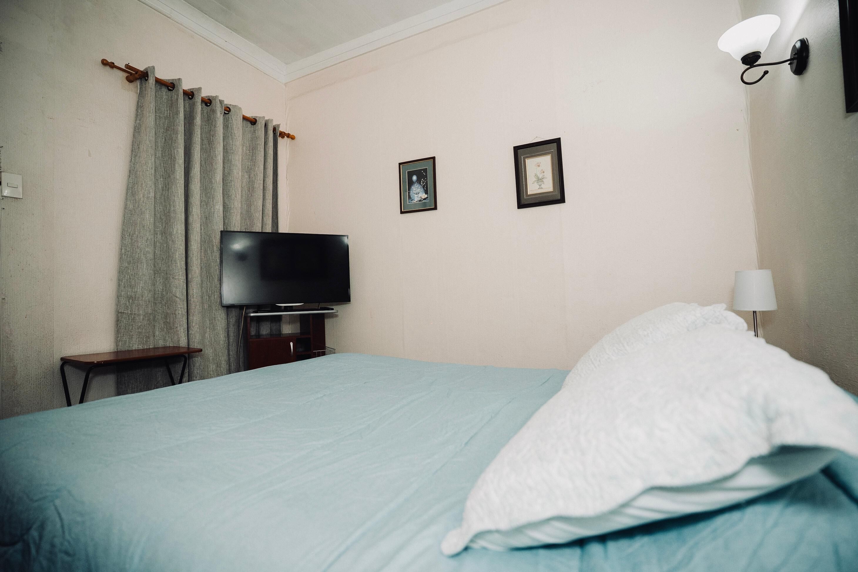 Een hotelkamer met een bed, een televisie, een klein tafeltje en twee foto's in lijsten aan de muur.