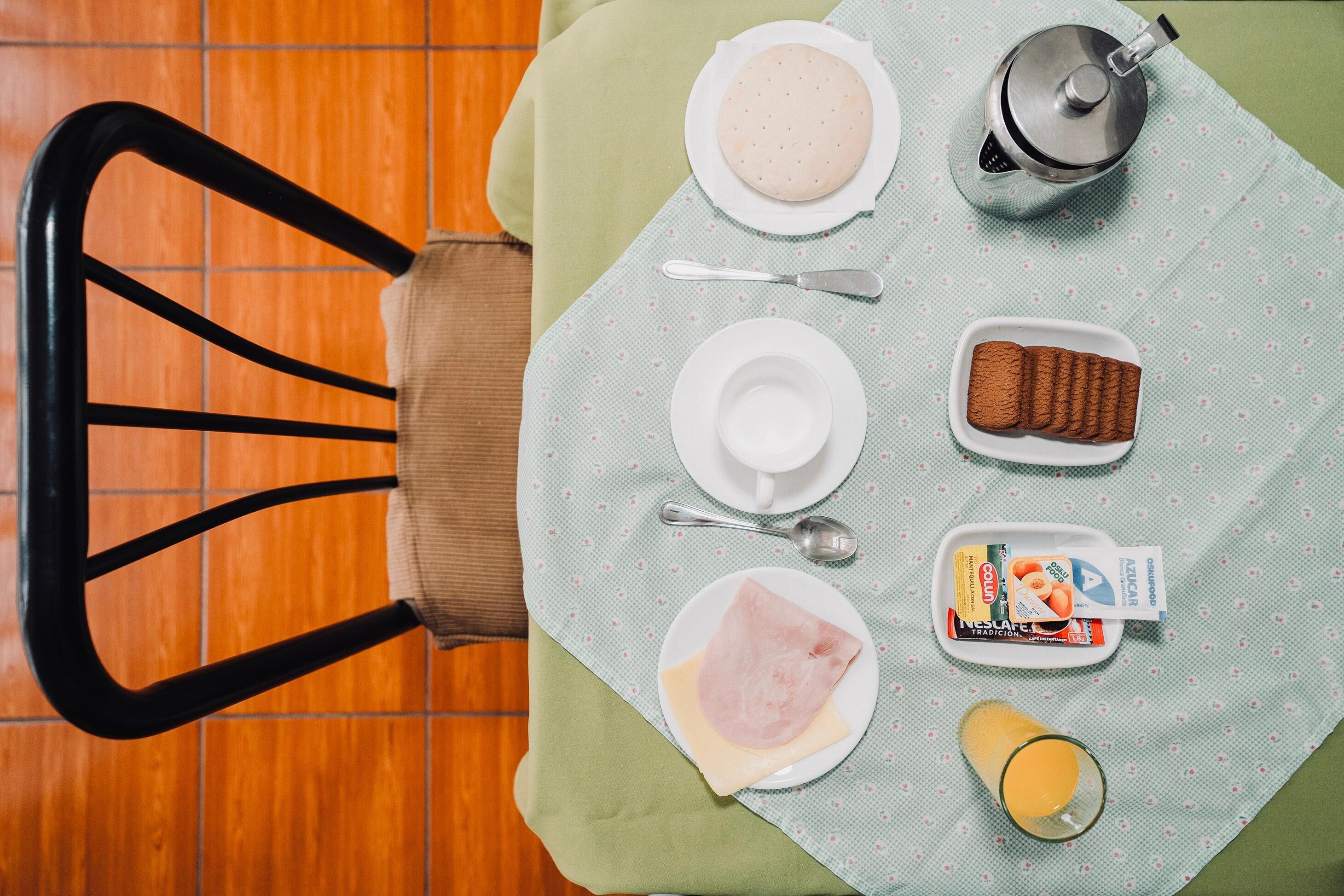 A breakfast setup with a plate of eggs, toast, a glass of orange juice, a coffee pot, and a packet of sugar.