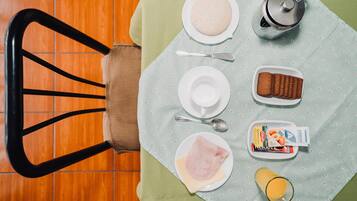Desayuno con un plato de huevos, tostadas, un vaso de jugo de naranja, una cafetera y un sobre de azúcar.