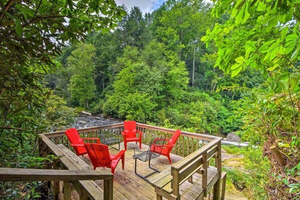 A wooden deck with red chairs and a table, surrounded by lush greenery and a waterfall. - Quiet Riverfront Retreat, 3 Decks, Lake/Kayaks (Jackson County)