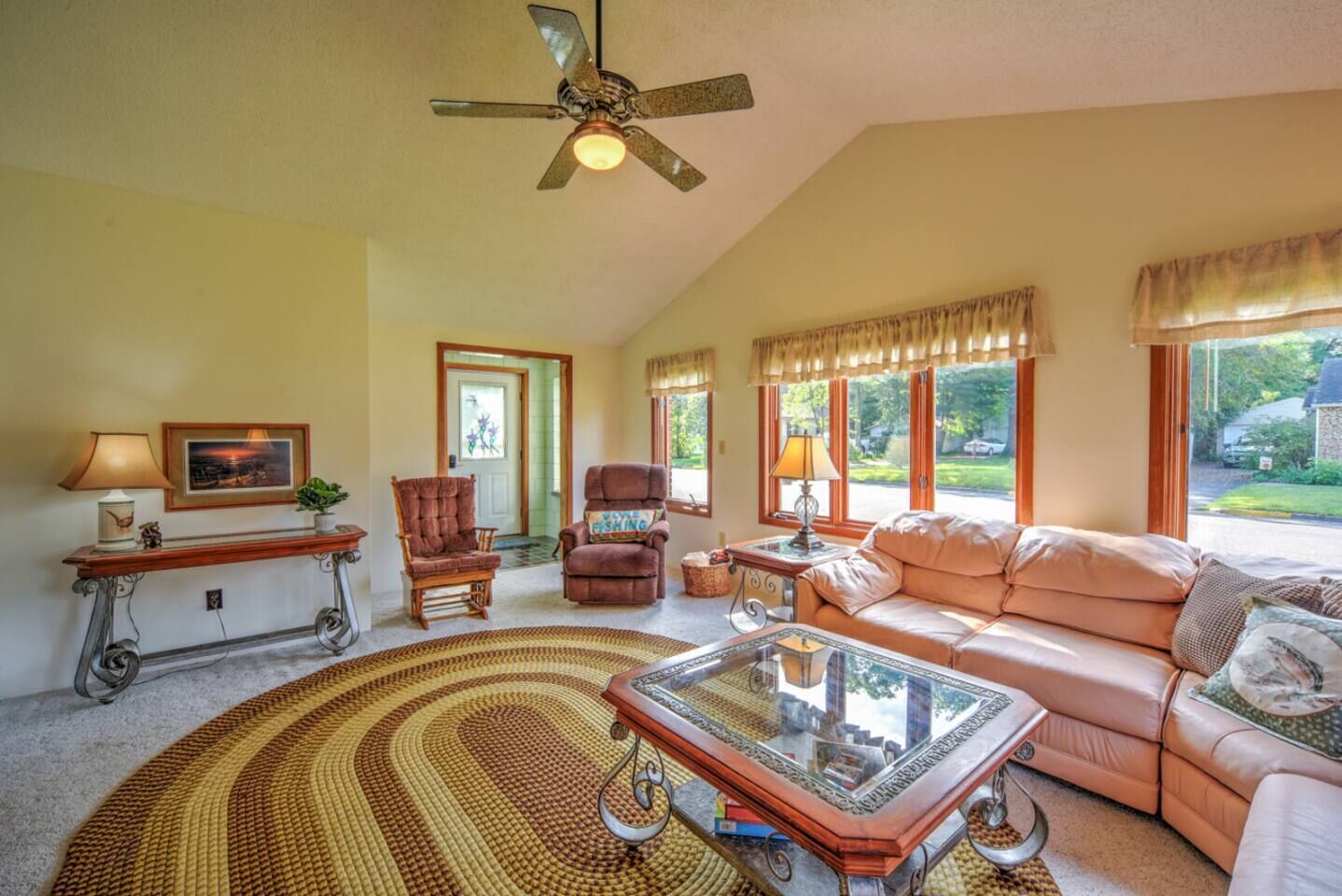 Un salon spacieux doté d’un grand ventilateur de plafond, d’une grande fenêtre avec des rideaux, d’un canapé, d’une table basse et de deux fauteuils.
