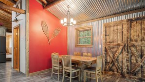 Un coin repas avec une table et des chaises en bois, un mur d’accent de couleur rouge et une porte en bois rustique.