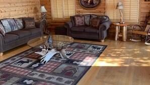 Interior de cabana de madeira com soalho de madeira, dois sofás, mesa de centro, ventoinha no teto e claraboia.