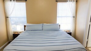 Un letto con copriletto a righe, due comodini e una finestra con tende.