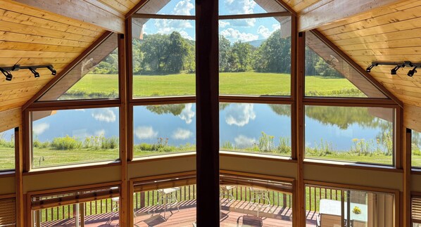 Habitación con ventanas amplias que ofrecen vistas a un lago y vegetación circundante.