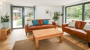 Una sala de estar moderna con un sofá de cuero marrón, una mesa de centro de madera y ventanas amplias que dan a un jardín.