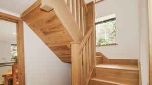 Una escalera de madera con barandilla que lleva a un rellano con ventana que da a zonas verdes.
