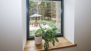 Una ventana con vista a un patio, que incluye una mesa, sillas y una planta en maceta sobre un repisa de madera.