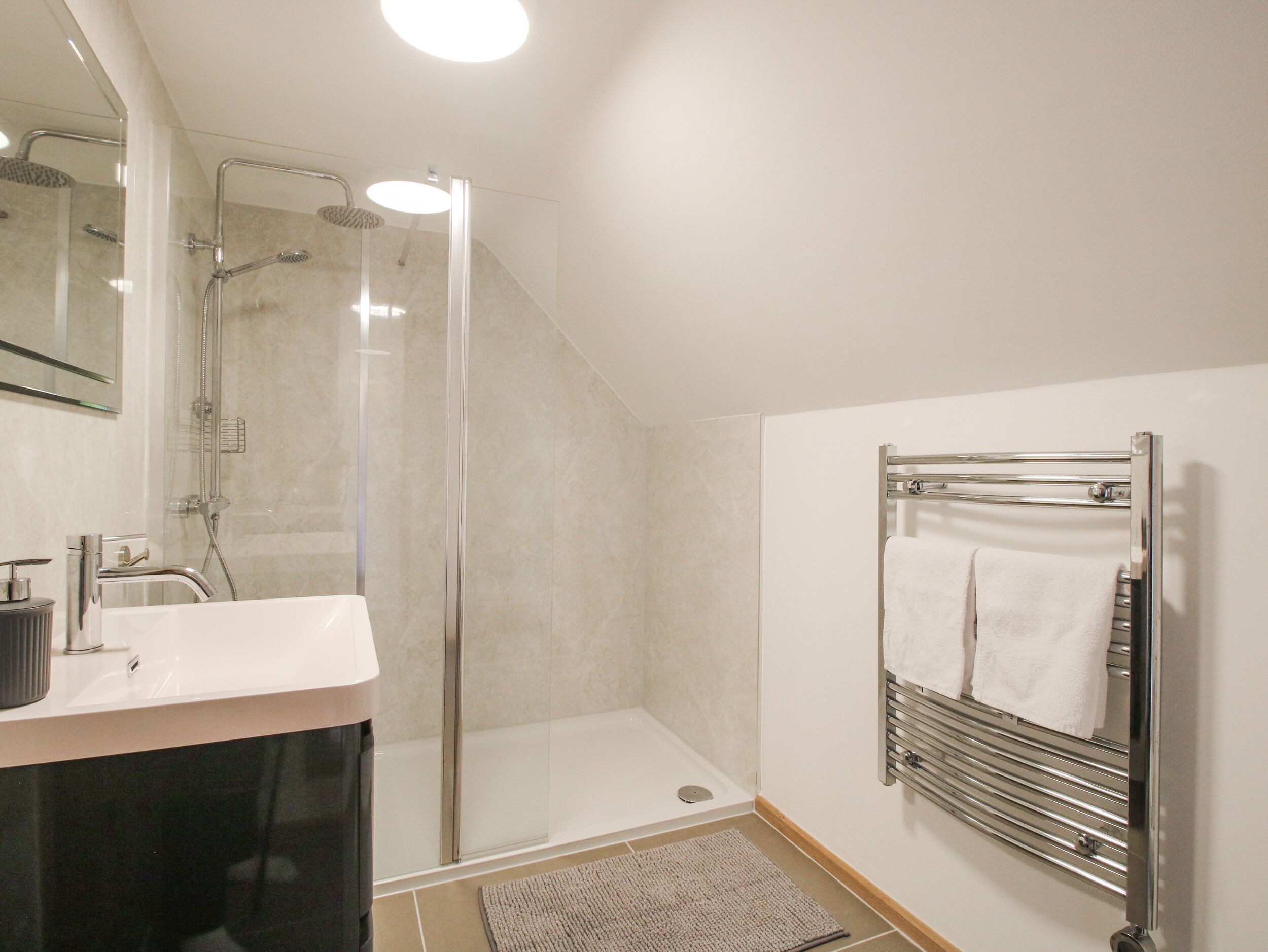 A modern bathroom with a glass-enclosed shower, a vanity with a sink, and a towel rack with two white towels.
