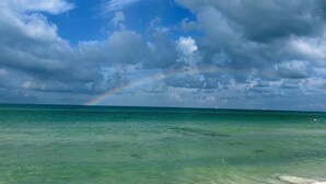 A clear view of the ocean with a rainbow and clouds in the sky.