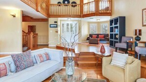 A spacious living area with a high ceiling, wooden staircase, and a balcony.
