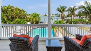 A covered outdoor area with wicker furniture, a pool, and a view of the marina and ocean.