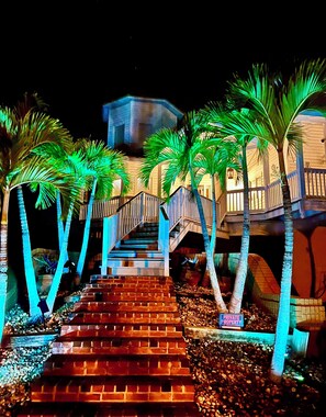 Una escalera que lleva a un edificio con un letrero de propiedad privada, rodeado de palmeras e iluminado por luces artificiales.