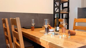 Una mesa de madera con sillas, una botella de vino, copas, un bol de fruta y dados.