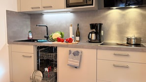 A modern kitchen with a dishwasher, a coffee maker, and fresh vegetables on the counter.