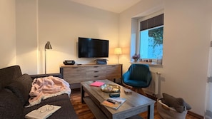 A living room with a sofa, a coffee table, a TV, a lamp, and a window with blinds.