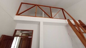 A room with a wooden loft structure, a staircase, and a door leading to another room.