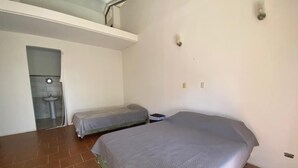 A bedroom with a single bed, a small bedside table, a wall-mounted light, and a window with a view of a building.