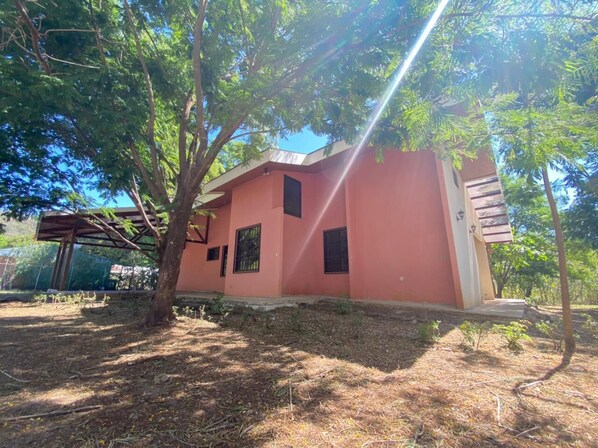 A single-story building with a pink facade, a small porch, and a covered outdoor seating area.