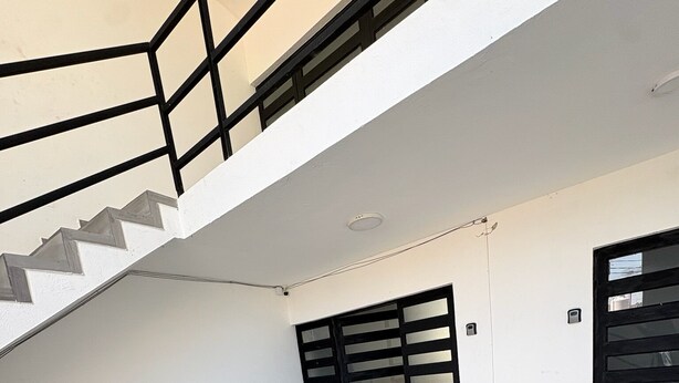 A staircase with a black railing, leading to a landing with a black door. - Residencia Gran Coyula Orange 512 (Tonalá)
