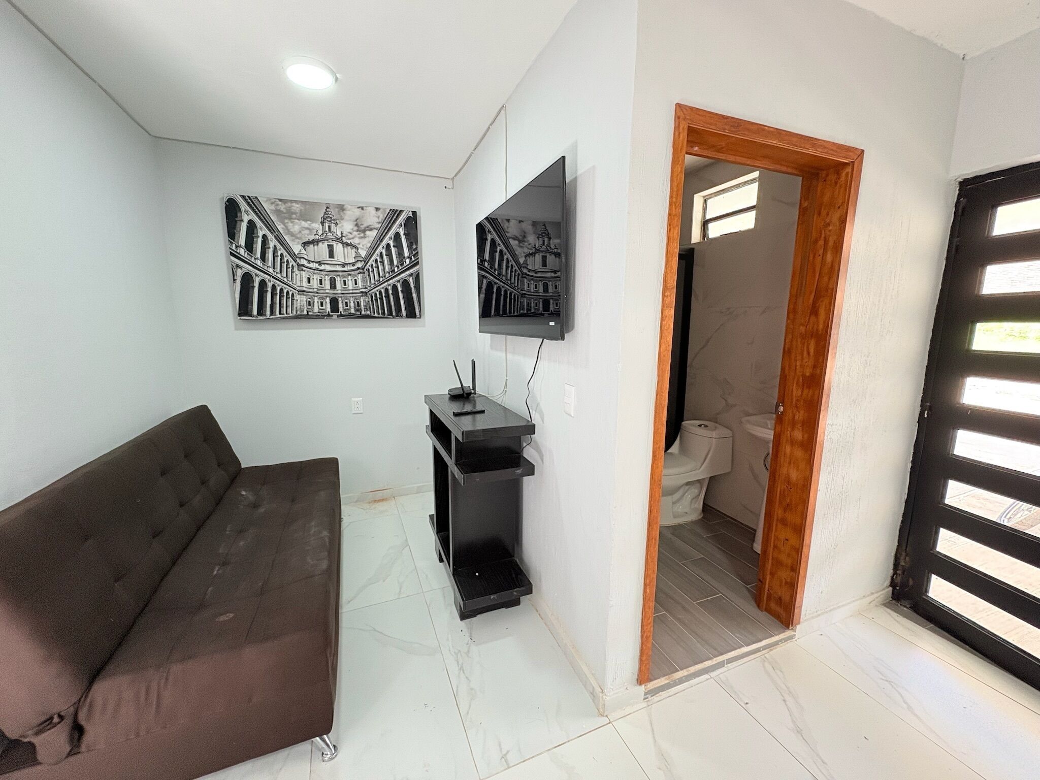Uma sala de estar com um sofá marrom, um rack preto e duas fotos emolduradas em preto e branco na parede.