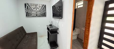 Uma sala de estar com um sofá marrom, um rack preto e duas fotos emolduradas em preto e branco na parede.