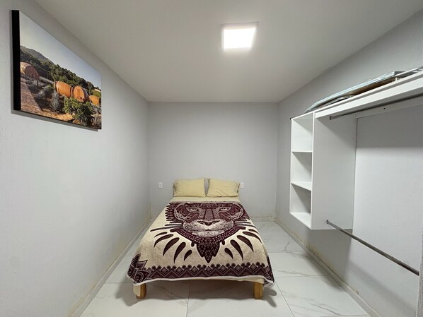 A small, narrow room with a bed, a white wardrobe, and a painting on the wall. - Residencia Gran Coyula Orange 512 (Tonalá)