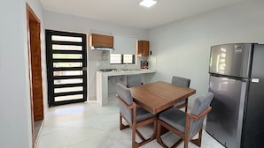 A compact kitchen with a dining table and chairs, a refrigerator, and a window with blinds. - Residencia Gran Coyula Orange 512 (Tonalá)