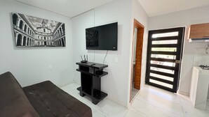 A living room with a flat-screen TV mounted on the wall, a black entertainment unit, a brown sofa, and a large framed picture of a historical building. - Residencia Gran Coyula Orange 512 (Tonalá)