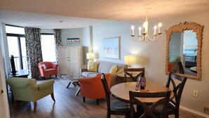 A living room with a sofa, chairs, a dining table, and a chandelier. - Our Newest Premium Ocean View Property - 2BR/2BA: Sleeps 8 - Top Amenities! (Myrtle Beach)