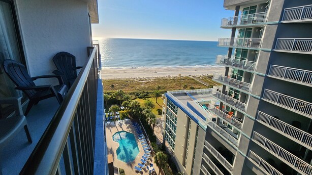 A balcony with chairs overlooking a swimming pool and beach. - Our Newest Premium Ocean View Property - 2BR/2BA: Sleeps 8 - Top Amenities! (Myrtle Beach)
