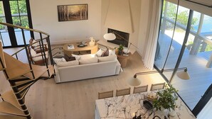 A spacious living area with a white sofa, a marble coffee table, and a dining area with a marble top. There is a staircase leading to a balcony with a view of greenery. - Don Pedro Island: Canal w. dock and 5-Min to Beach (Englewood)