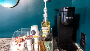 Eine Küchenarbeitsplatte mit einer Kaffeemaschine, einer Flasche Monin French Vanilla Sirup sowie einem transparenten Aufbewahrungsbehälter für Gewürze und Küchenutensilien.