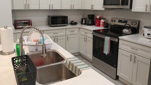A modern kitchen with white cabinets, a stainless steel sink, a microwave, a coffee maker, and a kettle. - beautiful vacation home (Ocala)