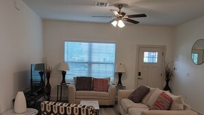 A living room with a sofa, armchair, and a TV on a stand. There is a ceiling fan and a window with blinds. - beautiful vacation home (Ocala)