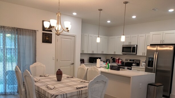 A modern kitchen with white cabinets, stainless steel appliances, and a dining area with a table and chairs. - beautiful vacation home (Ocala)