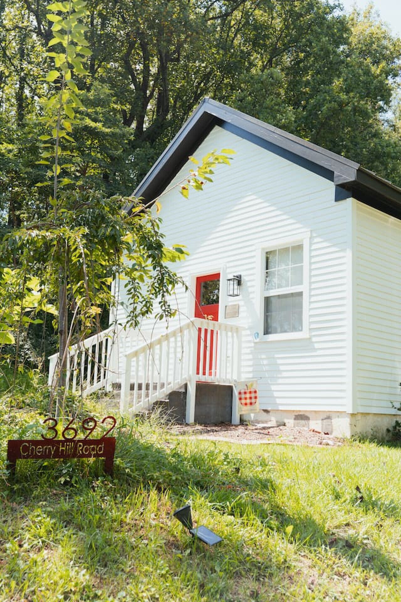 A white house with a red door, a porch, and a sign reading "3692 Cherry Hill Road".