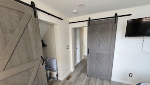 A room with a large sliding barn door, a bed with a striped blanket, and a television mounted on the wall.