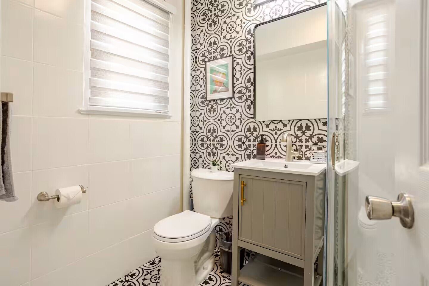 Un baño con inodoro, lavabo y espejo. Las paredes tienen un papel tapiz con diseño blanco y negro.