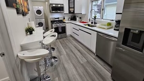 A modern kitchen with white cabinets, stainless steel appliances, a built-in oven, and a window with blinds.