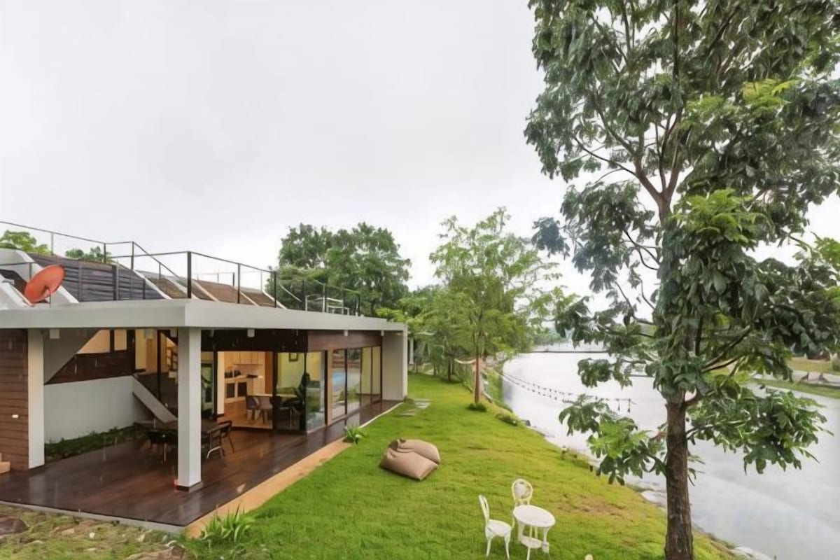 Een modern huis met een terras dat uitkijkt over een waterpartij, een trap en een eethoek.