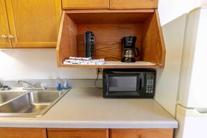 Een keuken met een houten kastje, een roestvrijstalen spoelbak, een magnetron en een koffiezetapparaat.