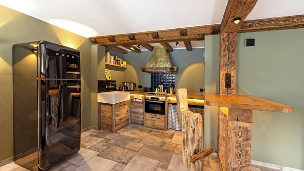 A kitchen with a built-in refrigerator, wooden beams, and a stone-tiled floor.