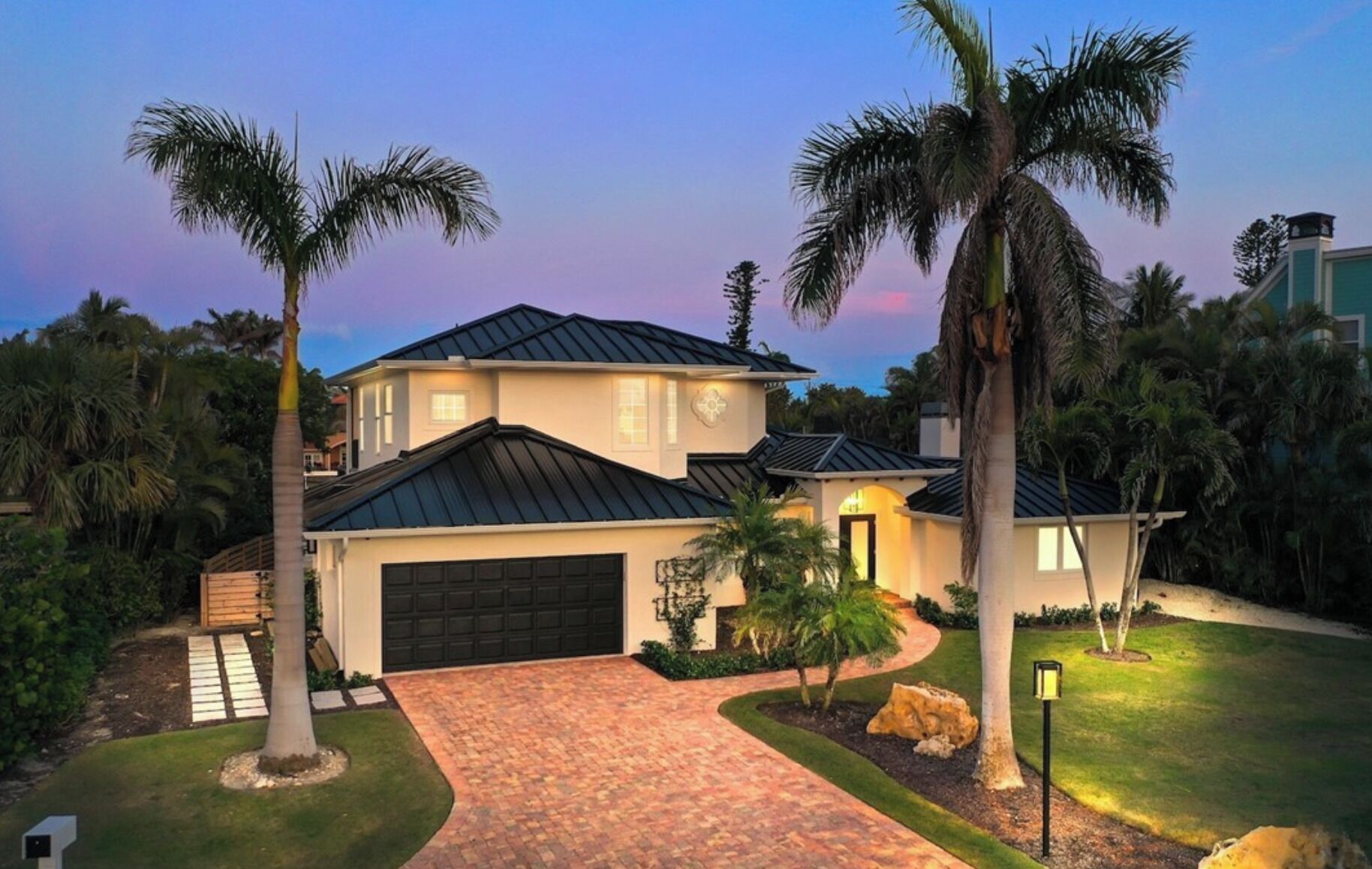 A two-story house with a black roof, a garage, and a paved driveway.