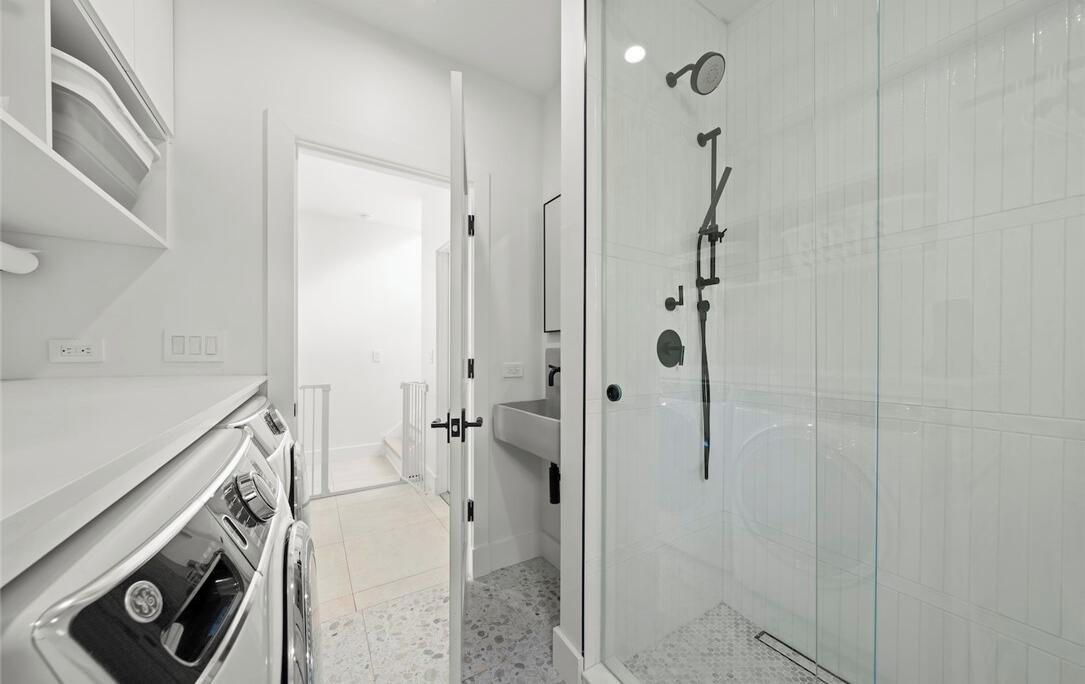 A modern bathroom with a glass shower enclosure, a white sink, and a white countertop with a built-in oven.