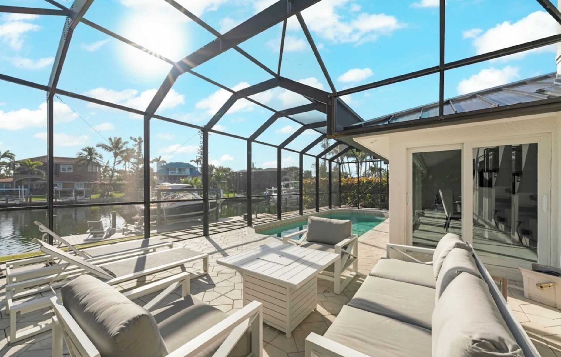 A covered outdoor area with a pool, lounge chairs, and a view of the water and surrounding houses.